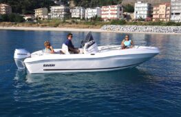 Lancha Ranieri navegando a baja velocidad en aguas tranquilas, con tres personas a bordo disfrutando del paseo. El diseño elegante del barco resalta en un entorno de montañas y costa en el fondo