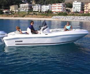 Lancha Ranieri navegando a baja velocidad en aguas tranquilas, con tres personas a bordo disfrutando del paseo. El diseño elegante del barco resalta en un entorno de montañas y costa en el fondo